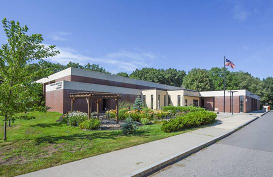 Sidewalk leading to the Colonie Library building showing green trees and blue sky