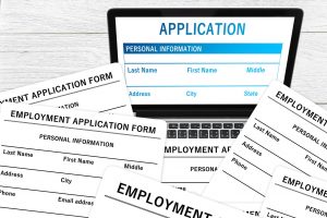 laptop with a job application on the screen and paper applications surrounding