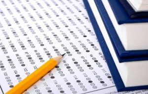 Scantron answer sheet with a yellow pencil and stack of blue books