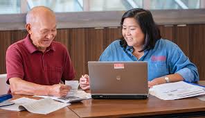 volunteer with a laptop assisting a person with paperword