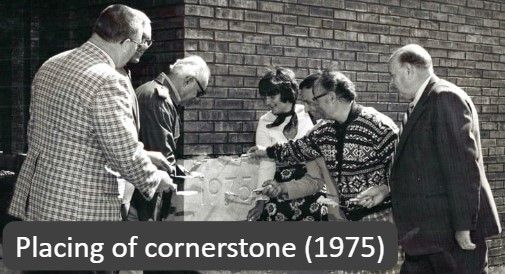 Black and white photo of six people around a cornerstone labeled 1975