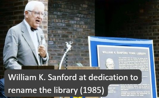 William K Sanford standing at a podium next to the library dedication plaque at the renaming in 1985