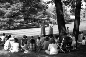 Two librarians standing and reading to a group of children outside
